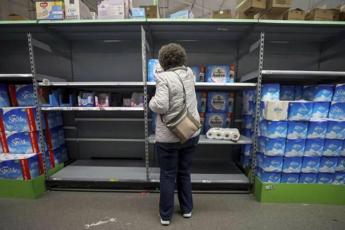 A customer selects an item from an almost empty section of toilet rolls at an Asda supermarket in England