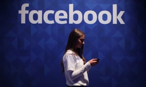 A woman using her phone under a Facebook logo.